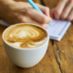 coffee cup, hand writing notes on a table